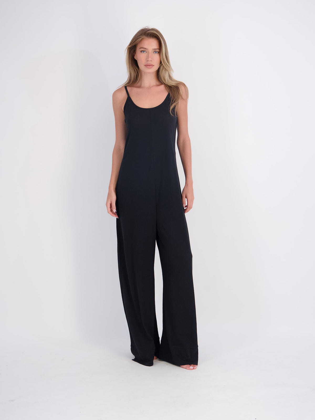 A woman modeling a black sleeveless jumpsuit with wide legs, standing against a plain white studio background.